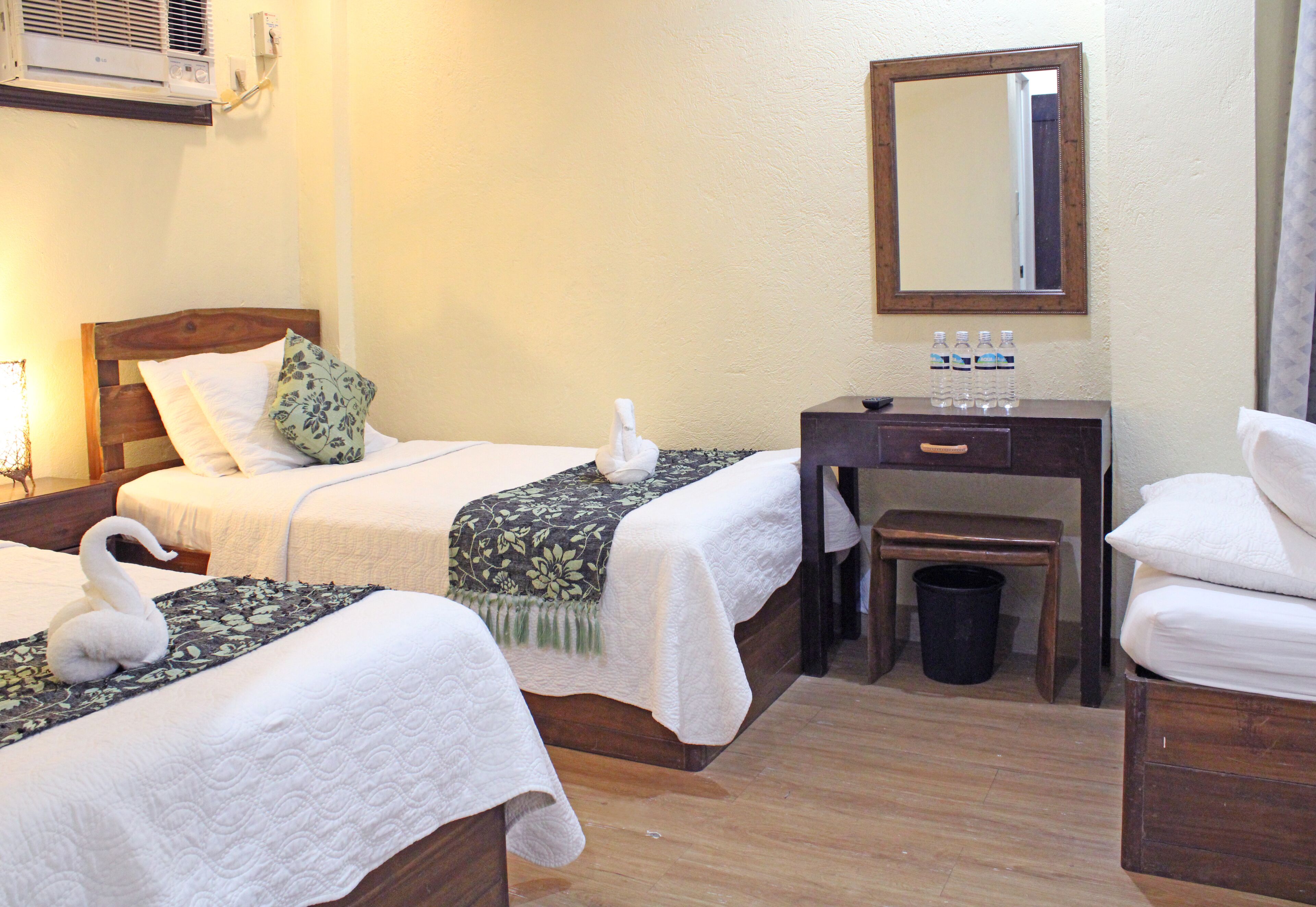Habitación de hotel con dos camas, un escritorio de madera, un espejo y un cesto de basura.