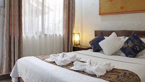 A hotel room with a neatly made bed, a nightstand with a lamp, and a decorative wall hanging. - Balaibinda Lodge (Coron)