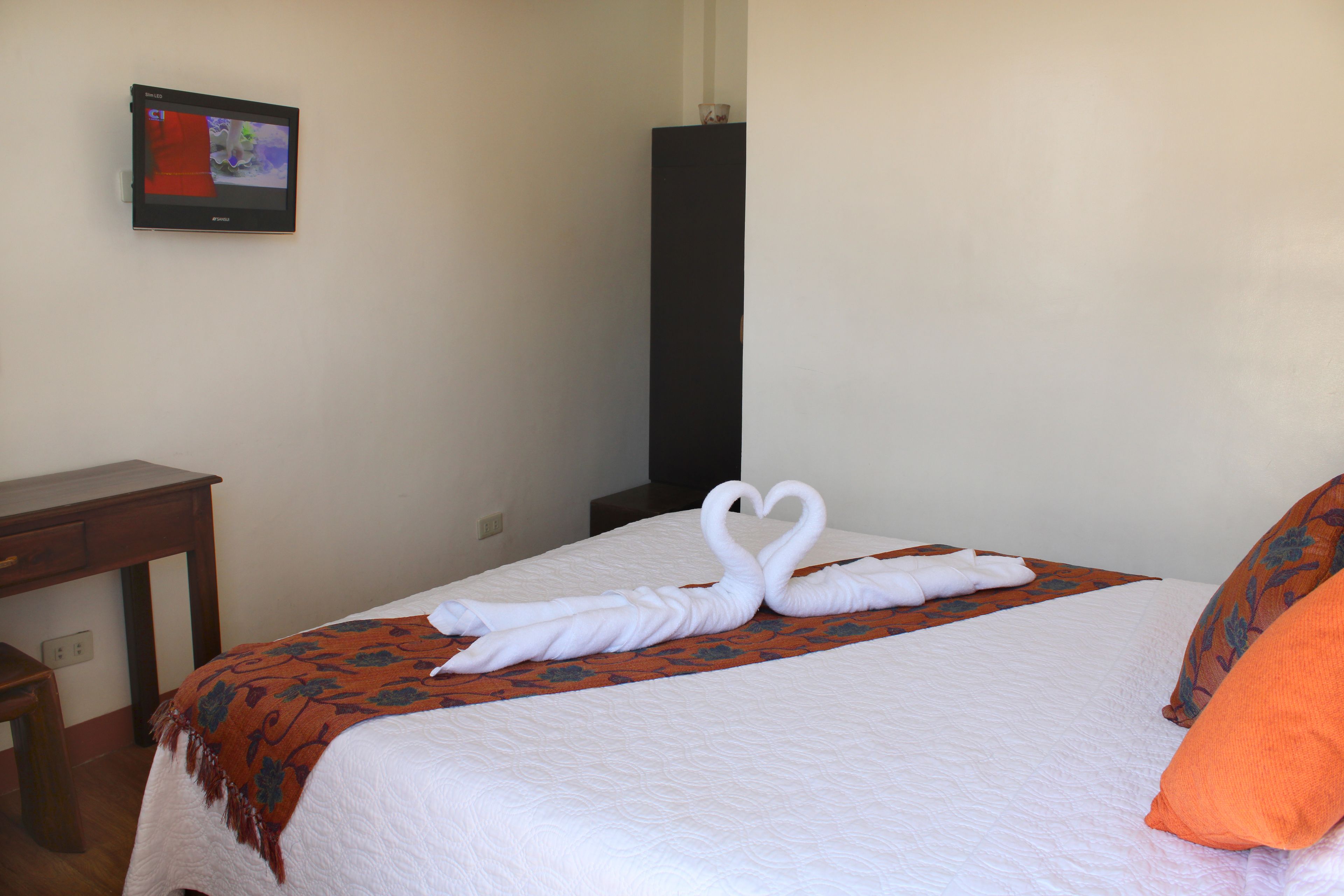 Una habitación de hotel con una cama bien hecha, un escritorio y un televisor montado en la pared.
