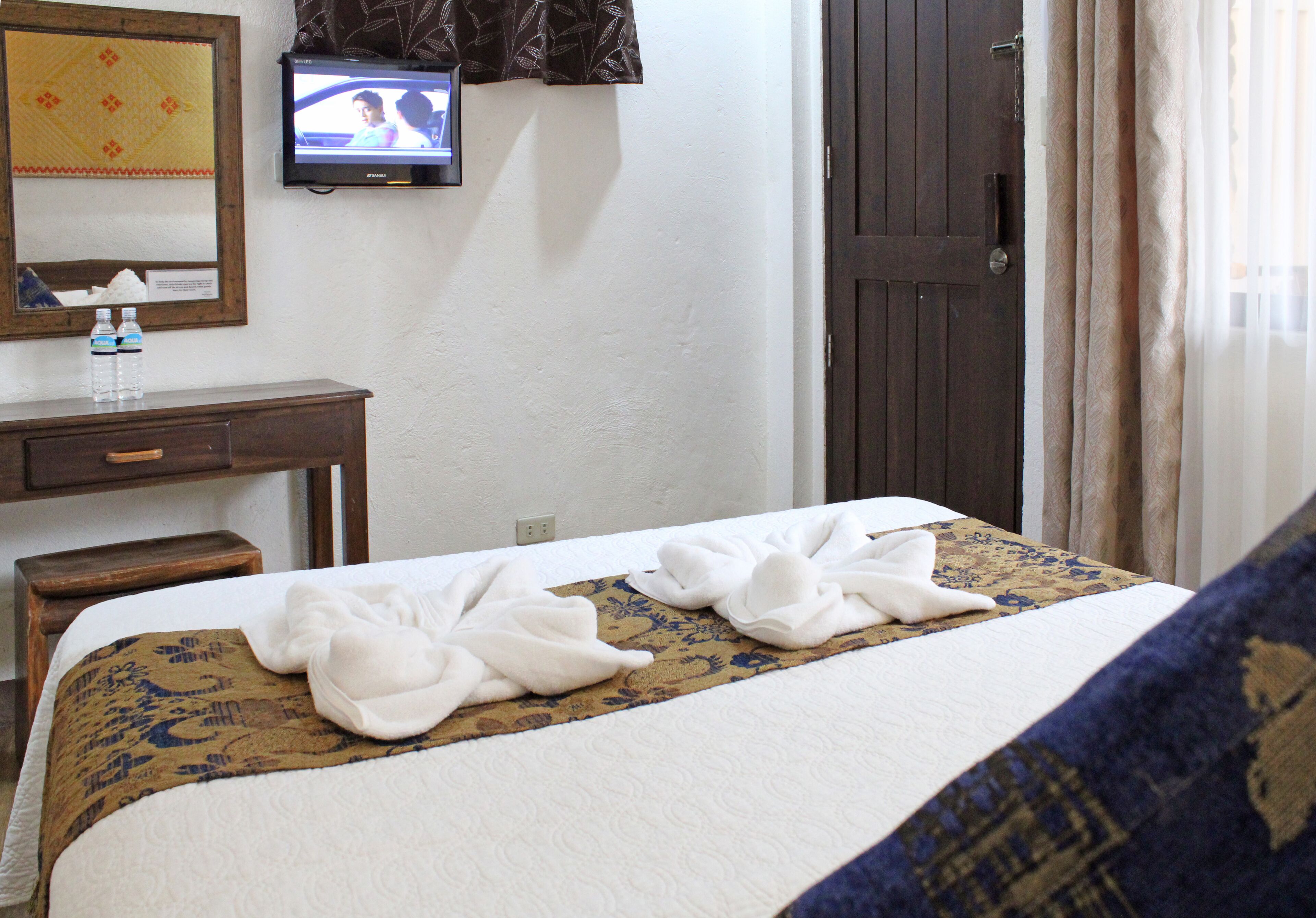 A hotel room with a bed, a television on the wall, a desk with a chair, and a door.