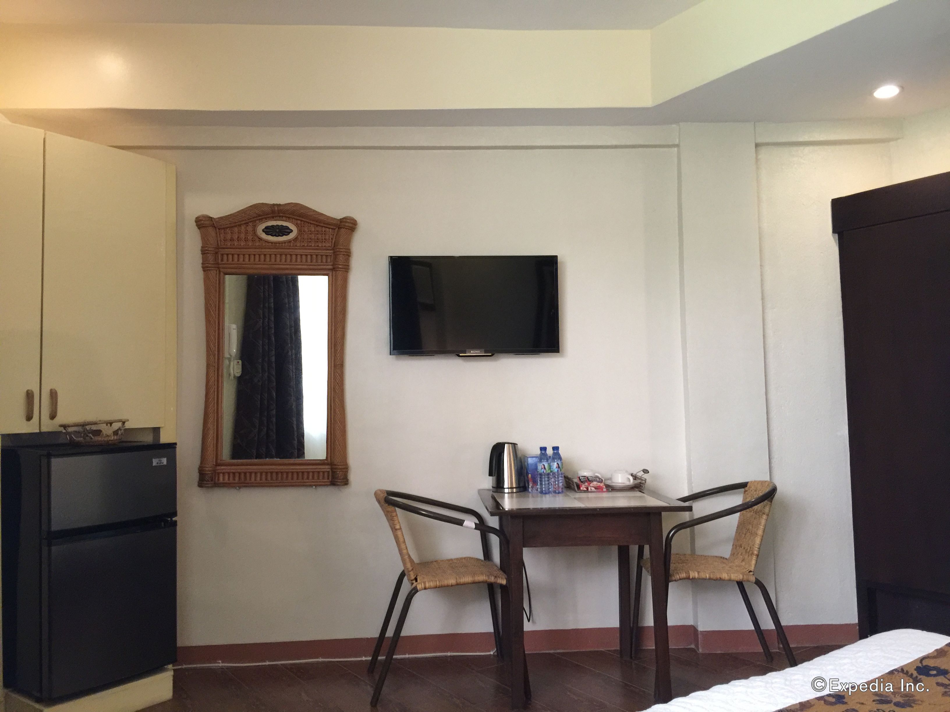 A hotel room with a bed, a TV, a small table with chairs, a mirror, and a minibar.