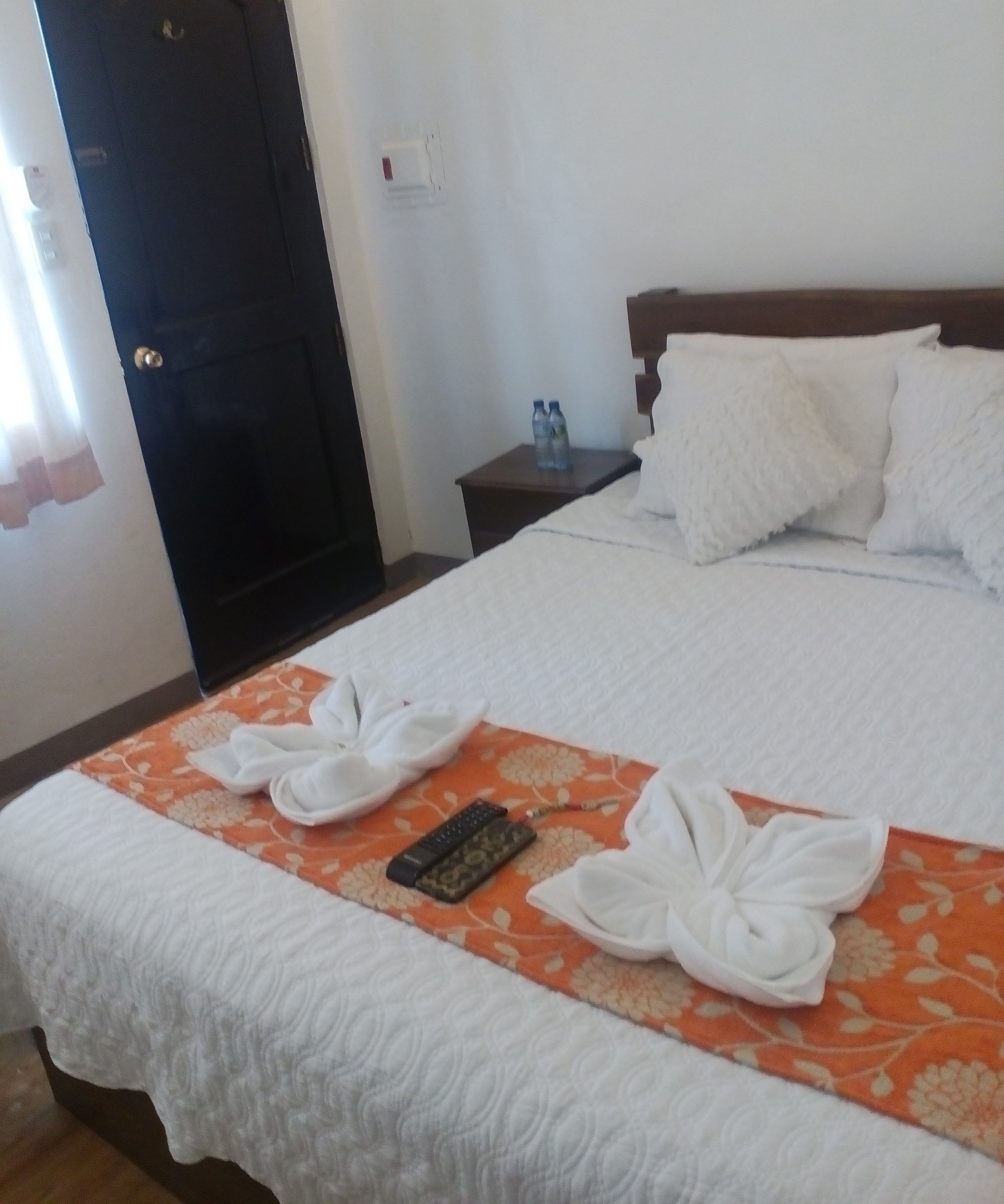 A hotel room with a bed, a nightstand, and a door.