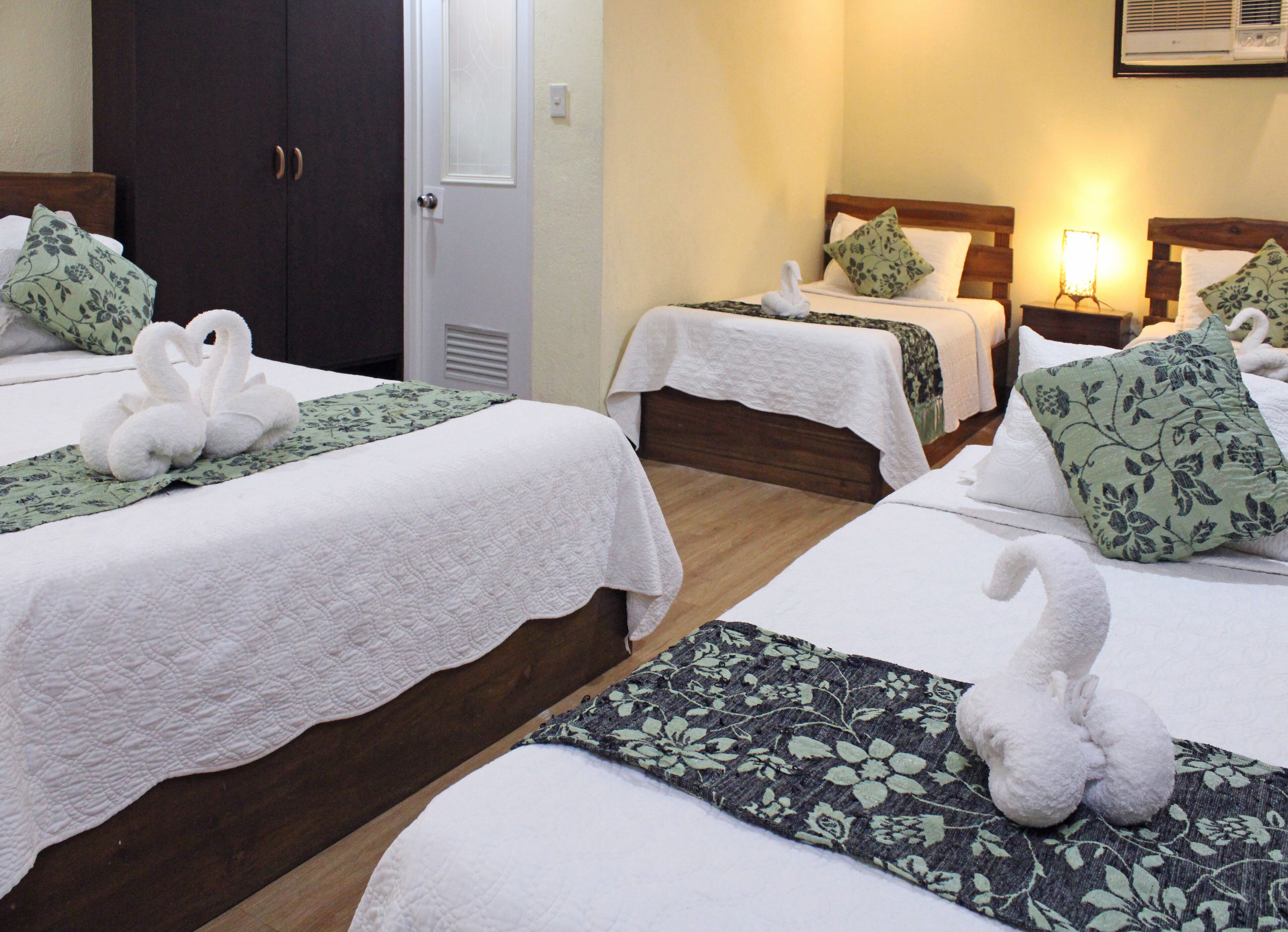 A hotel room with three beds, each with a white bedspread and decorative swan-shaped towels.