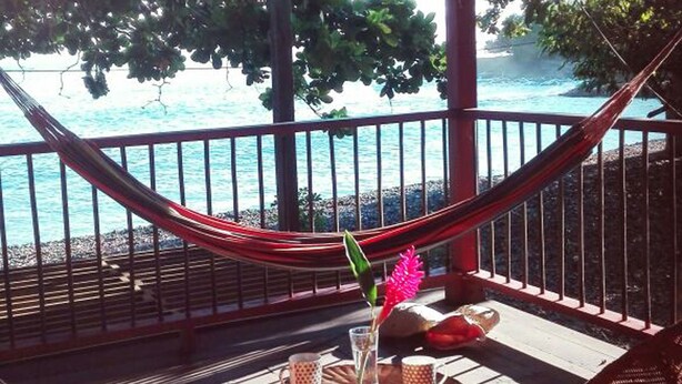 A covered outdoor area with a hammock, wicker chairs, and a table with a drink and a flower. - Finca El Regalo (Acandi)
