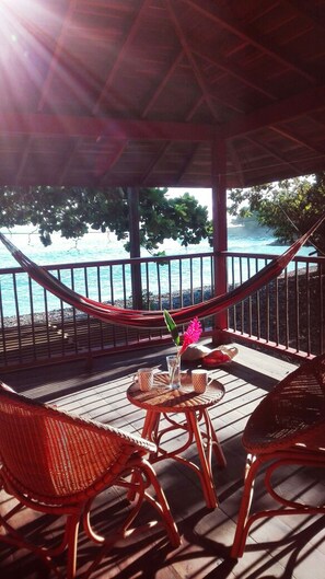 A covered outdoor area with a hammock, wicker chairs, and a table with a drink and a flower. - Finca El Regalo (Acandi)