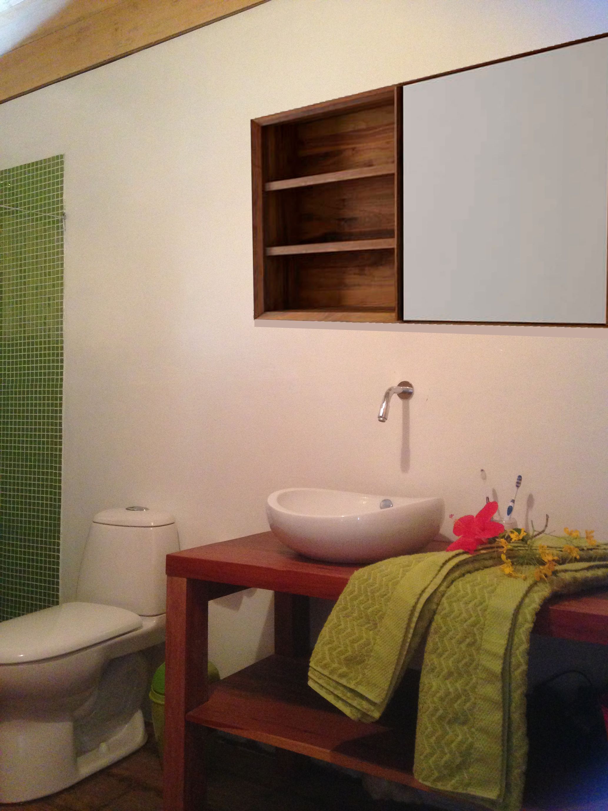 A bathroom with a white toilet, a wooden vanity with a white sink, and a green towel on the counter.