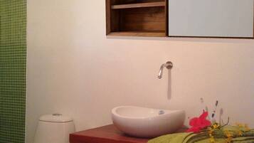 A bathroom with a white toilet, a wooden vanity with a white sink, and a green towel on the counter.