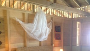 A wooden room with a bed, a hanging white cloth, and two wall-mounted lamps. - Finca El Regalo (Acandi)
