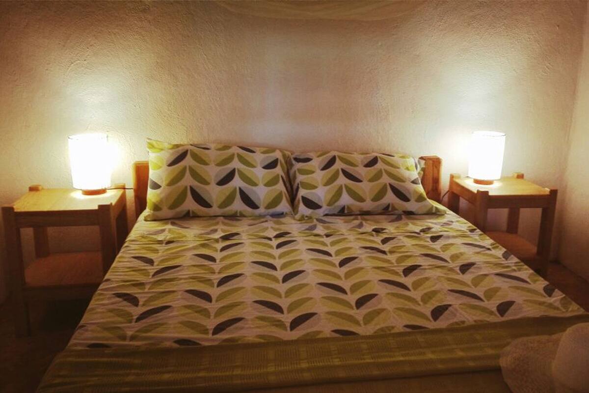 A bed with a leaf-patterned bedspread, two bedside lamps, and a wooden nightstand on each side.