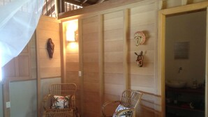 A room with two wicker chairs, a wooden floor, a staircase, and a bathroom visible through an open door. - Finca El Regalo (Acandi)