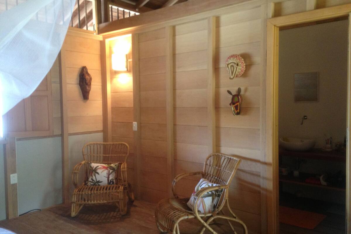 A room with two wicker chairs, a wooden floor, a staircase, and a bathroom visible through an open door.
