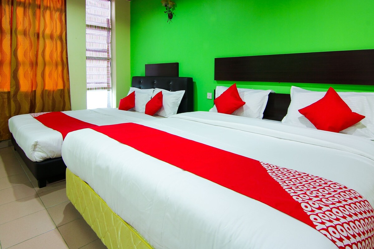 A hotel room with two beds, each with white bedding and red accents, a green wall, and a window with curtains.