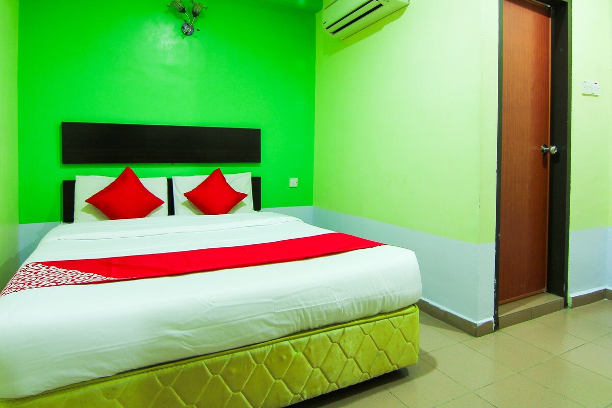 A hotel room with a bed, green walls, a wooden door, and an air conditioning unit.