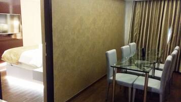 A hotel room with a glass dining table, four chairs, a bed with white bedding, a television, and a curtain.