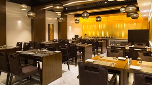 Um restaurante com várias mesas e cadeiras, um espaço de bar e iluminação pendente.