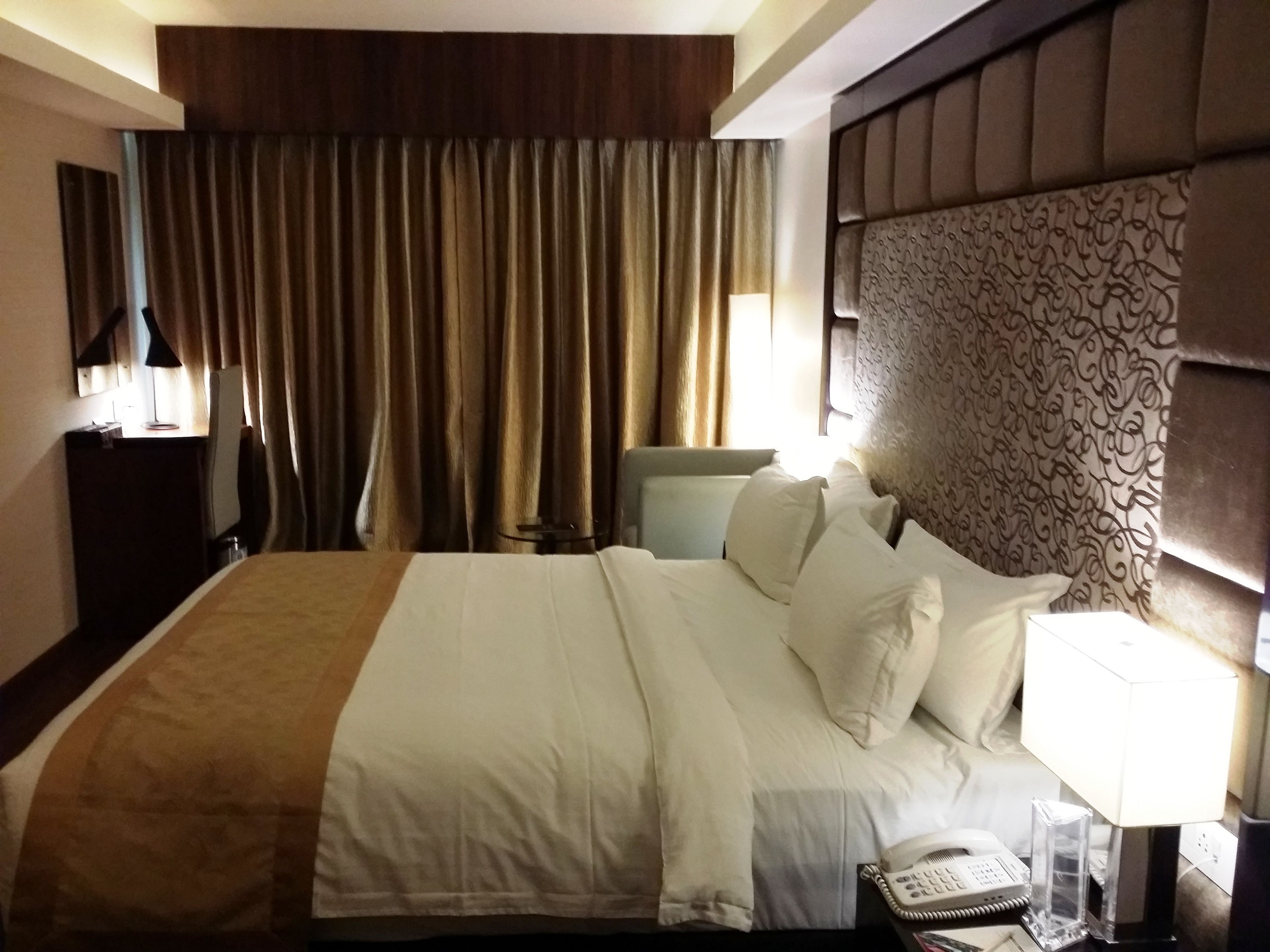 A hotel room with a large bed, a bedside table with a lamp, a telephone, and a chair.