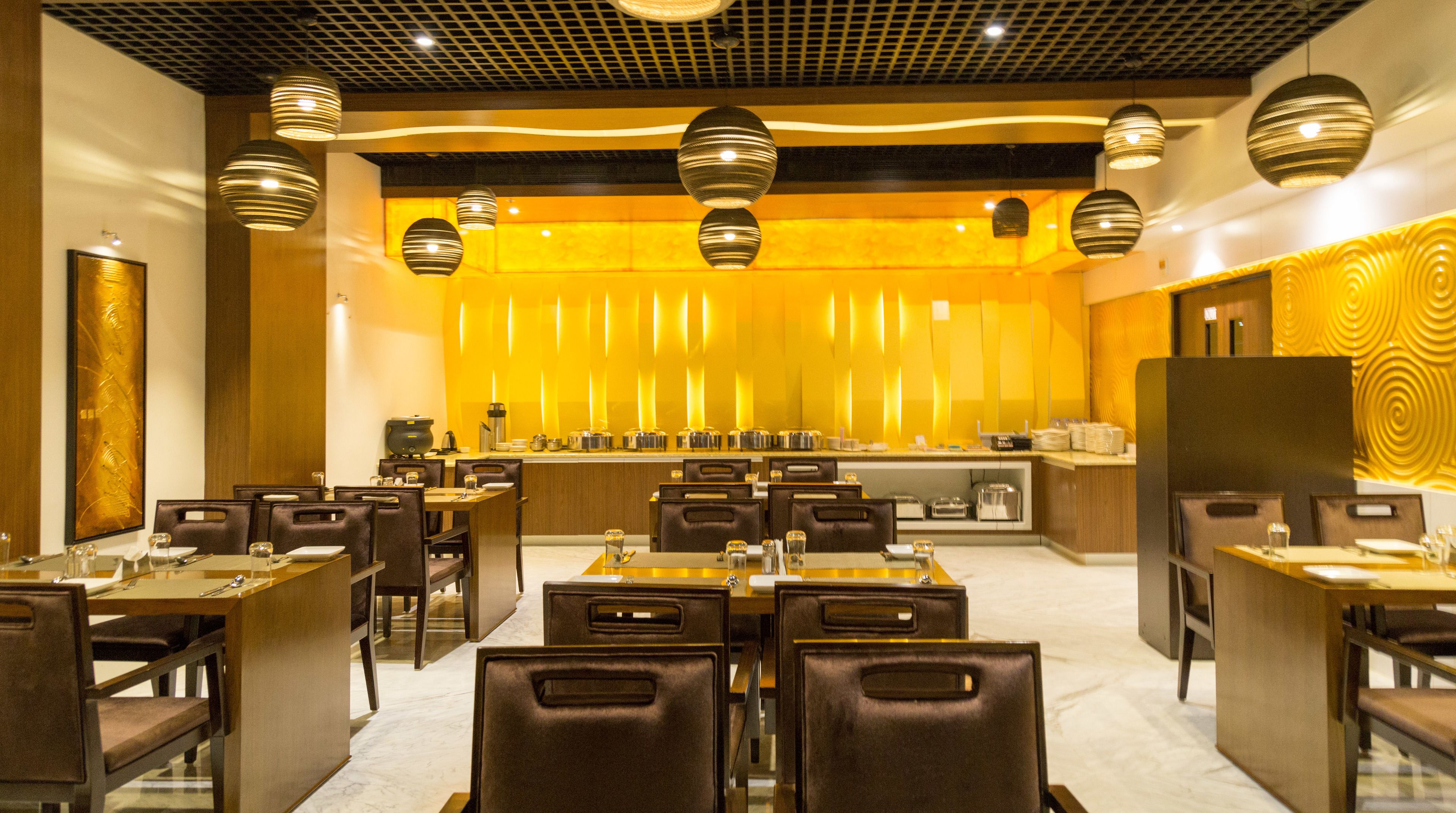 A modern dining area with multiple tables and chairs, a central counter with various appliances, and decorative lighting fixtures.