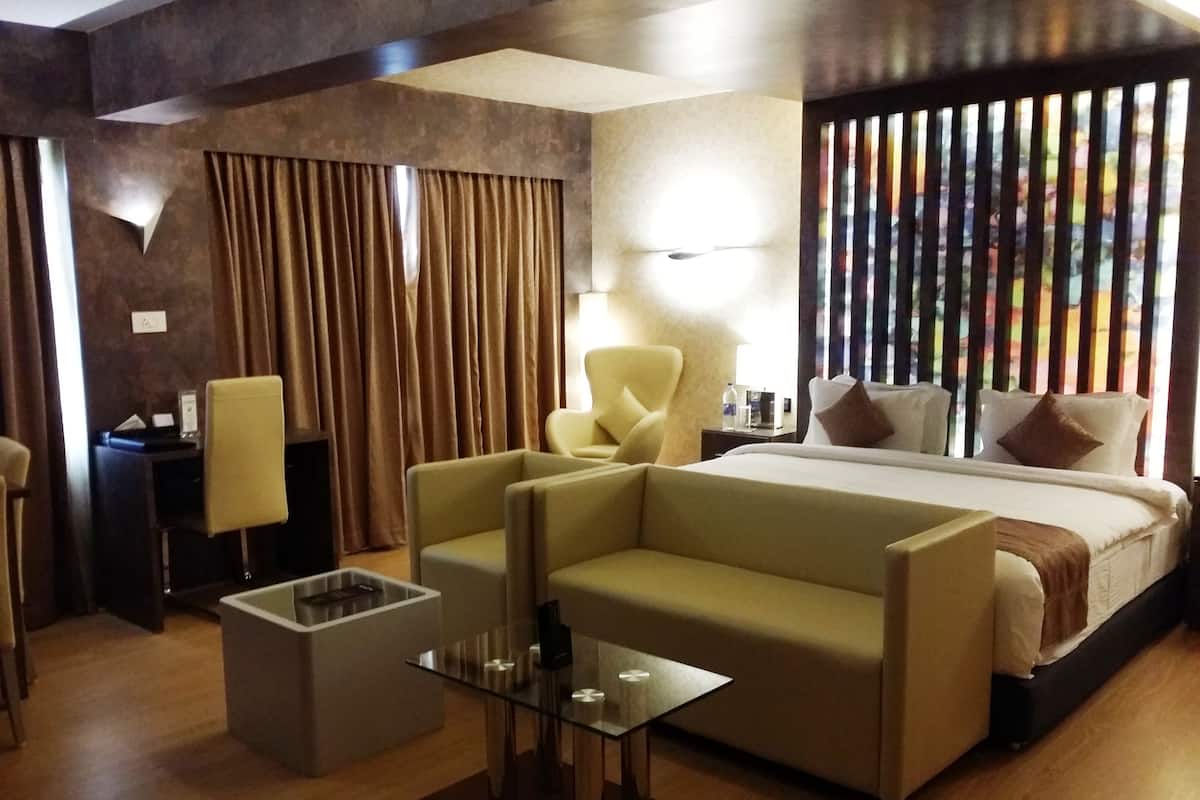 Una habitación de hotel moderna con una cama grande, dos sillones, una mesa de centro de cristal y un escritorio con lámpara.