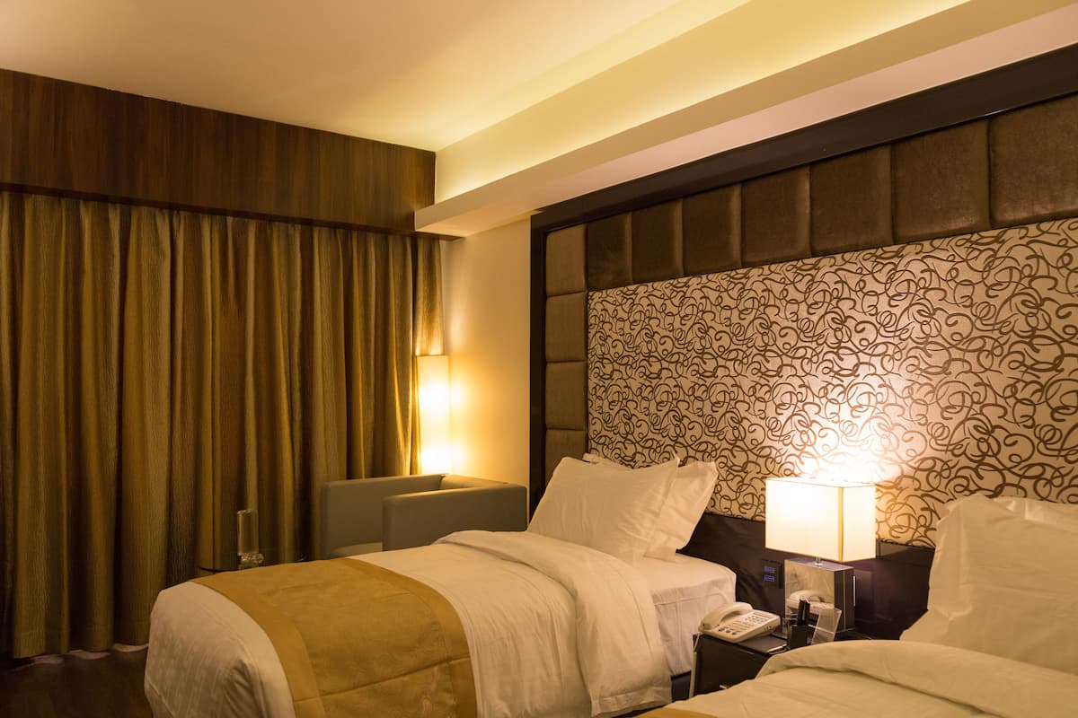 Una habitación de hotel con dos camas, un cabecero estampado y una mesita de noche con lámpara.