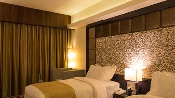 A hotel room with two beds, a patterned headboard, and a nightstand with a lamp.