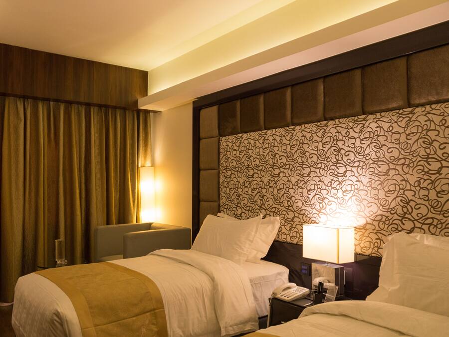 A hotel room with two beds, a patterned headboard, and a nightstand with a lamp.