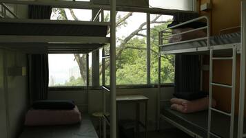 Habitación tipo dormitorio con literas, una mesita pequeña y ventana con vistas a árboles y edificios.