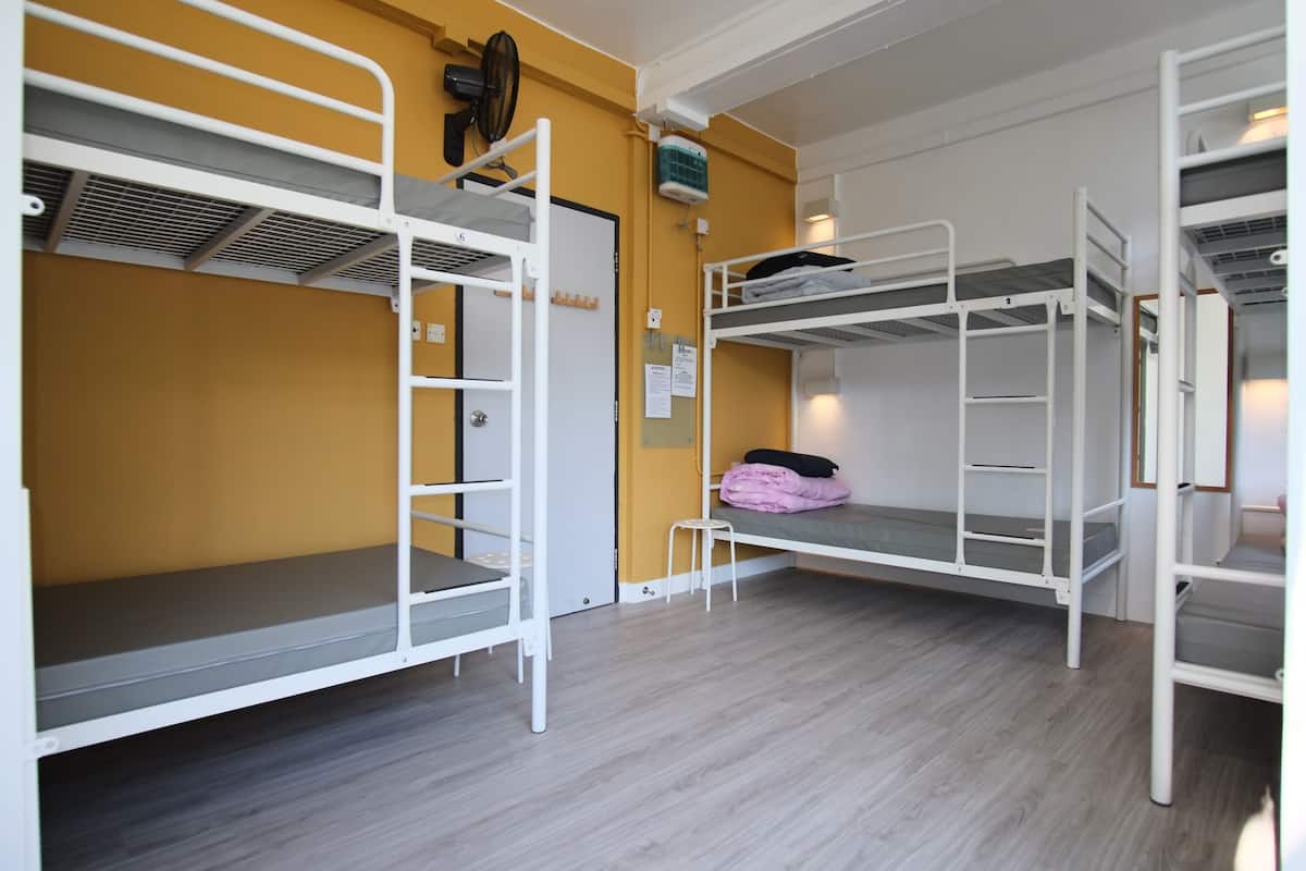 A dormitory room with bunk beds, a heater, and a small stool.