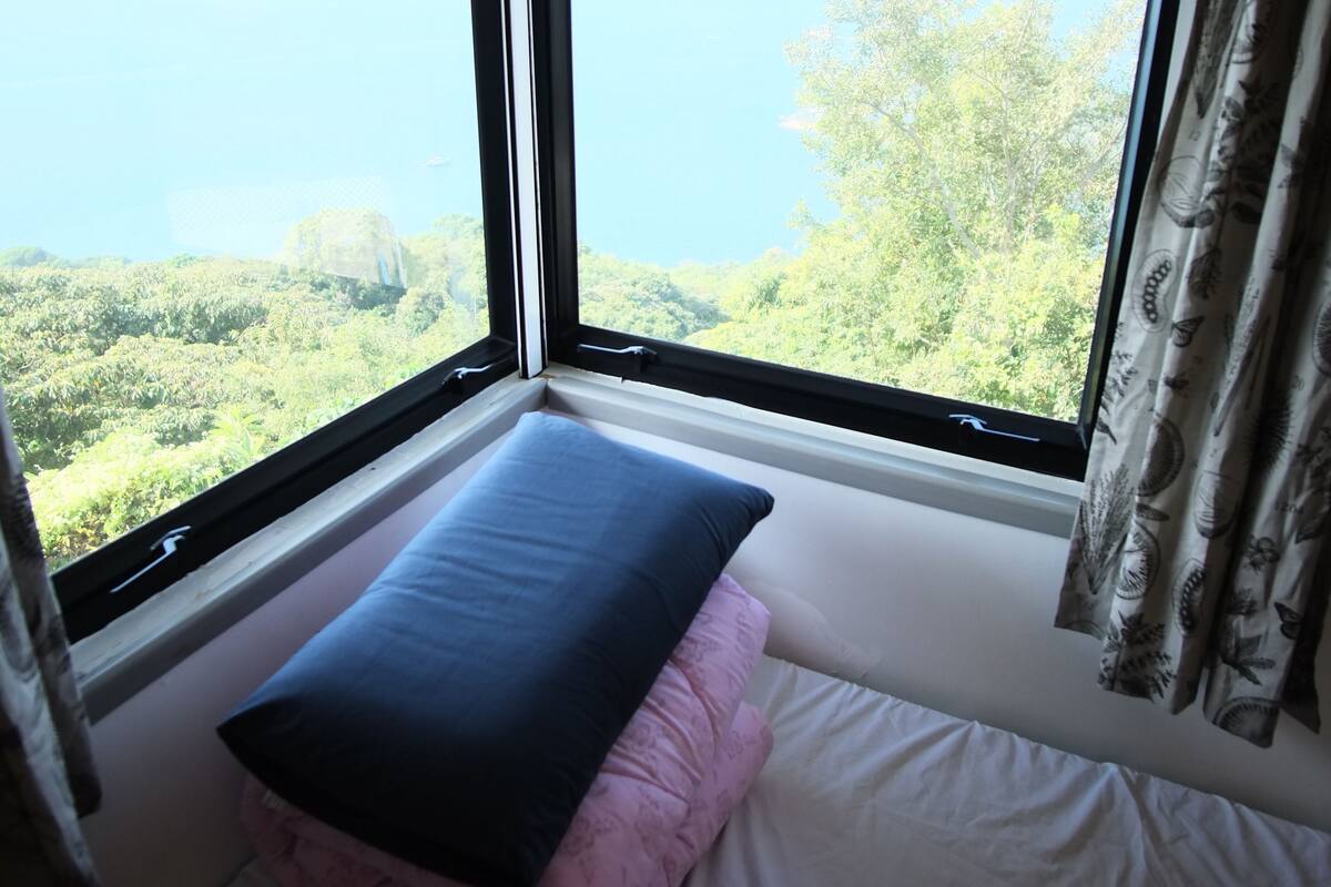 A room with a bed against a window overlooking a forested area.