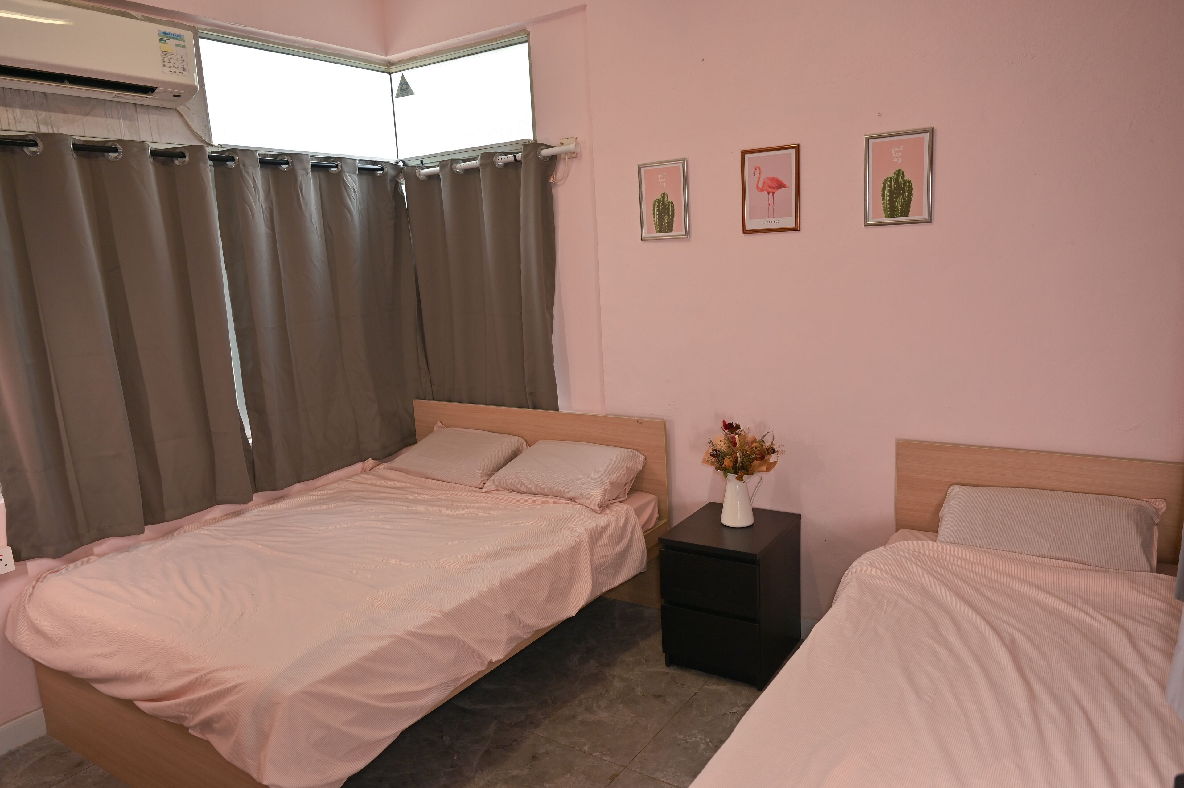 Un dormitorio con dos camas, una ventana con cortinas, un aire acondicionado instalado en la pared y tres cuadros enmarcados.