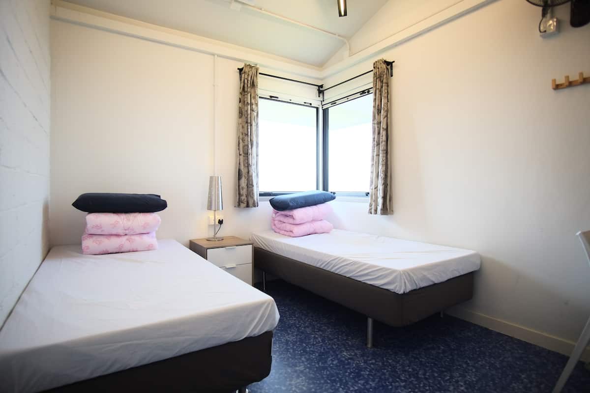 A small, clean room with two single beds, a nightstand, and a window with curtains.