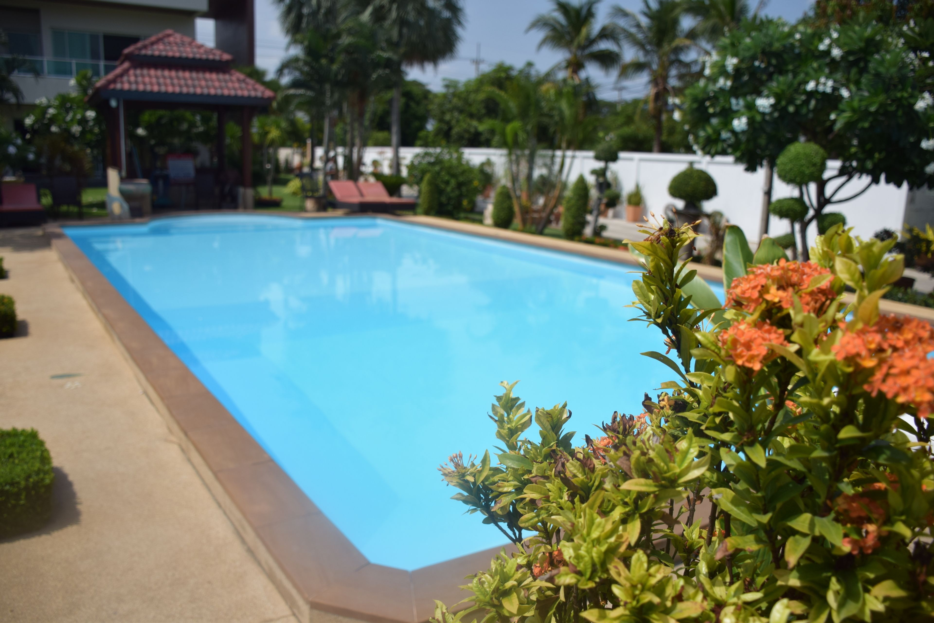 Una piscina con una terraza de baldosas, rodeada de follaje y un pabellón.