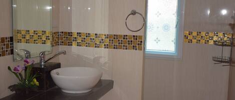 Un baño con un lavamanos blanco, un espejo y una ventana con un borde de azulejos decorativos.