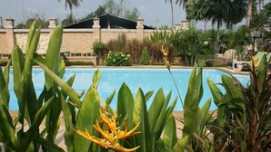 A swimming pool surrounded by lush greenery and a stone wall. - Sumali Villa (Sing Buri)