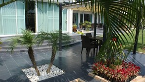 A patio area with palm trees, a table, and chairs. - Sumali Villa (Sing Buri)