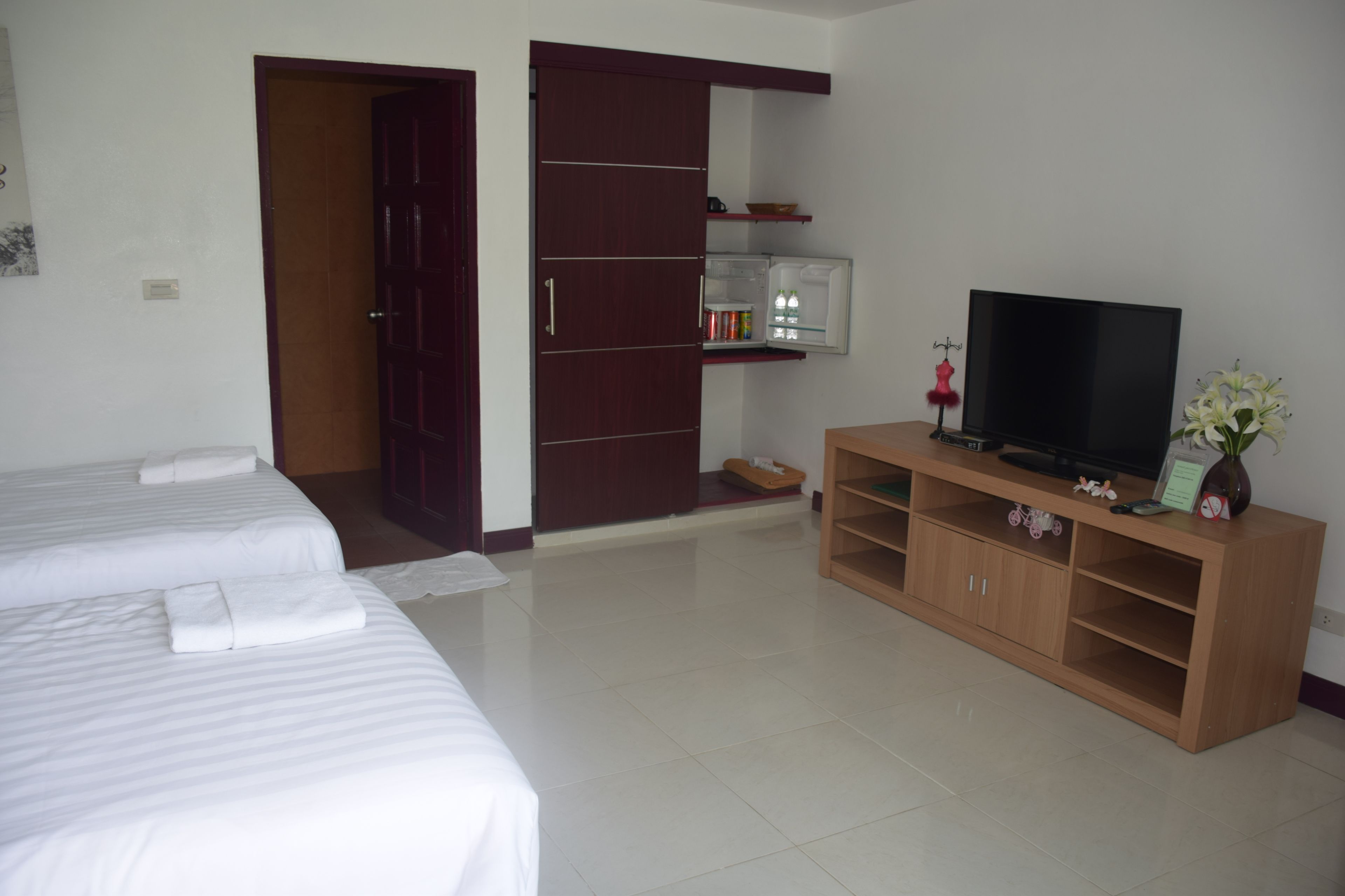 A hotel room with two beds, a TV on a wooden stand, a wardrobe, and a small shelf with toiletries.