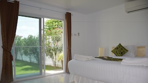 A bedroom with a large bed, a sliding glass door to a balcony, and a view of greenery outside. - Sumali Villa (Sing Buri)