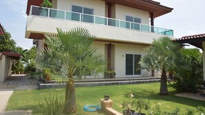 A two-story house with a balcony, surrounded by a well-maintained lawn and palm trees. - Sumali Villa (Sing Buri)