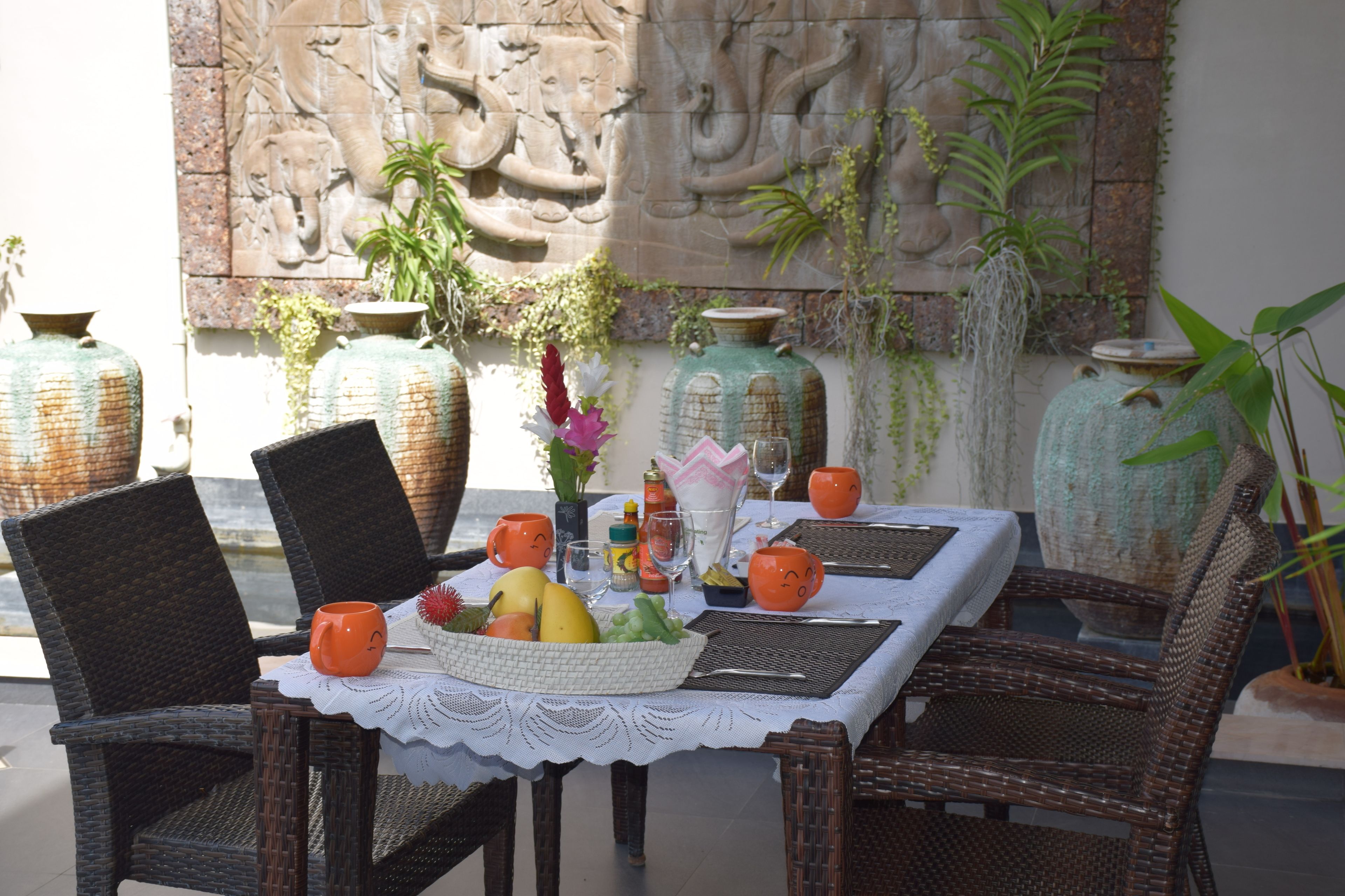 Una mesa de comedor con sillas de mimbre, una cesta de frutas y elementos decorativos.