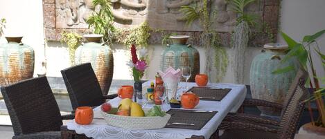 Una mesa de comedor con sillas de mimbre, una cesta de frutas y elementos decorativos.