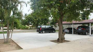 A parking area with a covered car wash station, a black minivan, and a tree-lined background.