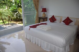Habitación de hotel con una cama grande, una mesita de noche con lámpara y vista a un jardín a través de un ventanal.