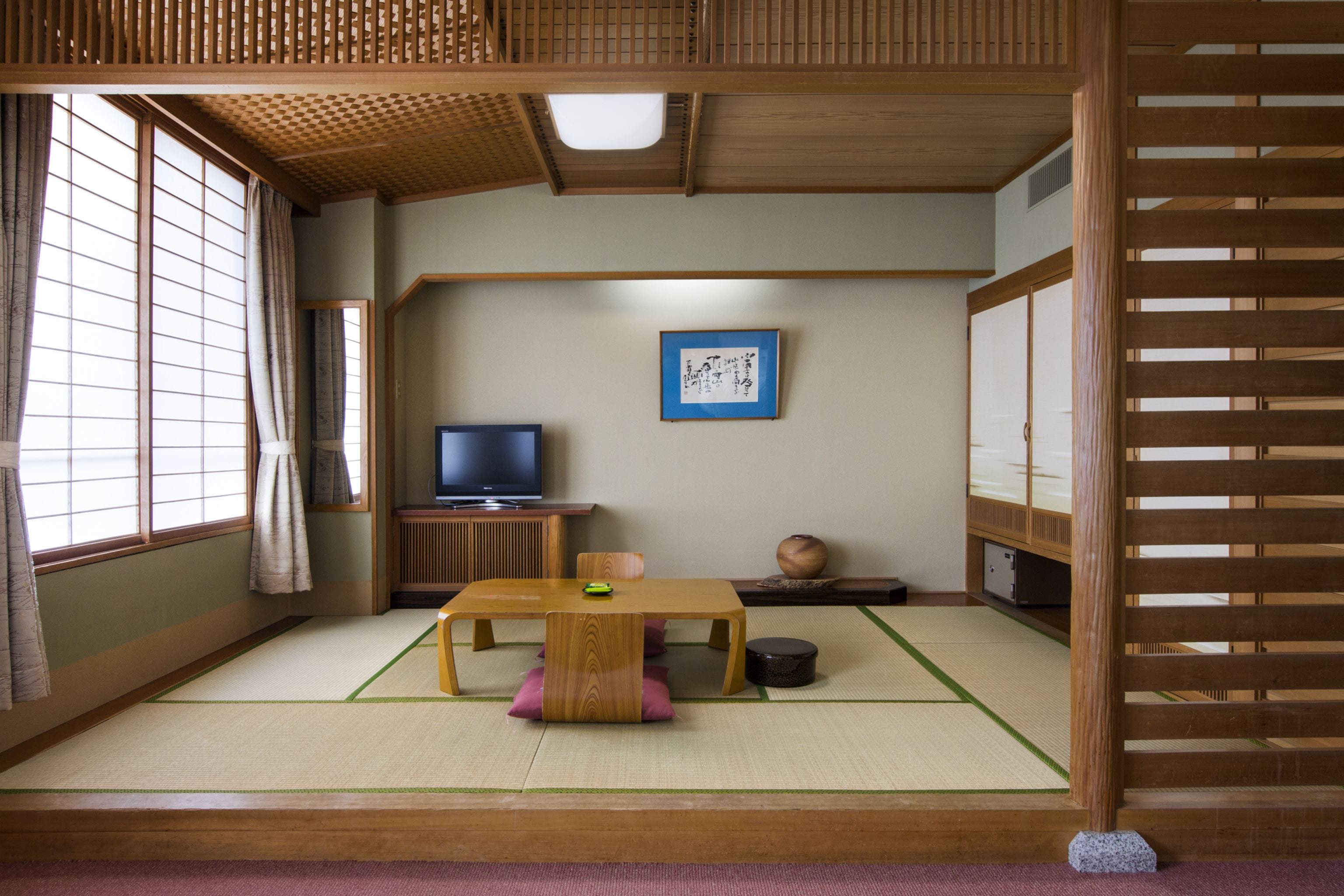 Une pièce de style japonais traditionnel, avec un sol recouvert de tatamis, une basse table en bois, un téléviseur et des portes coulissantes.