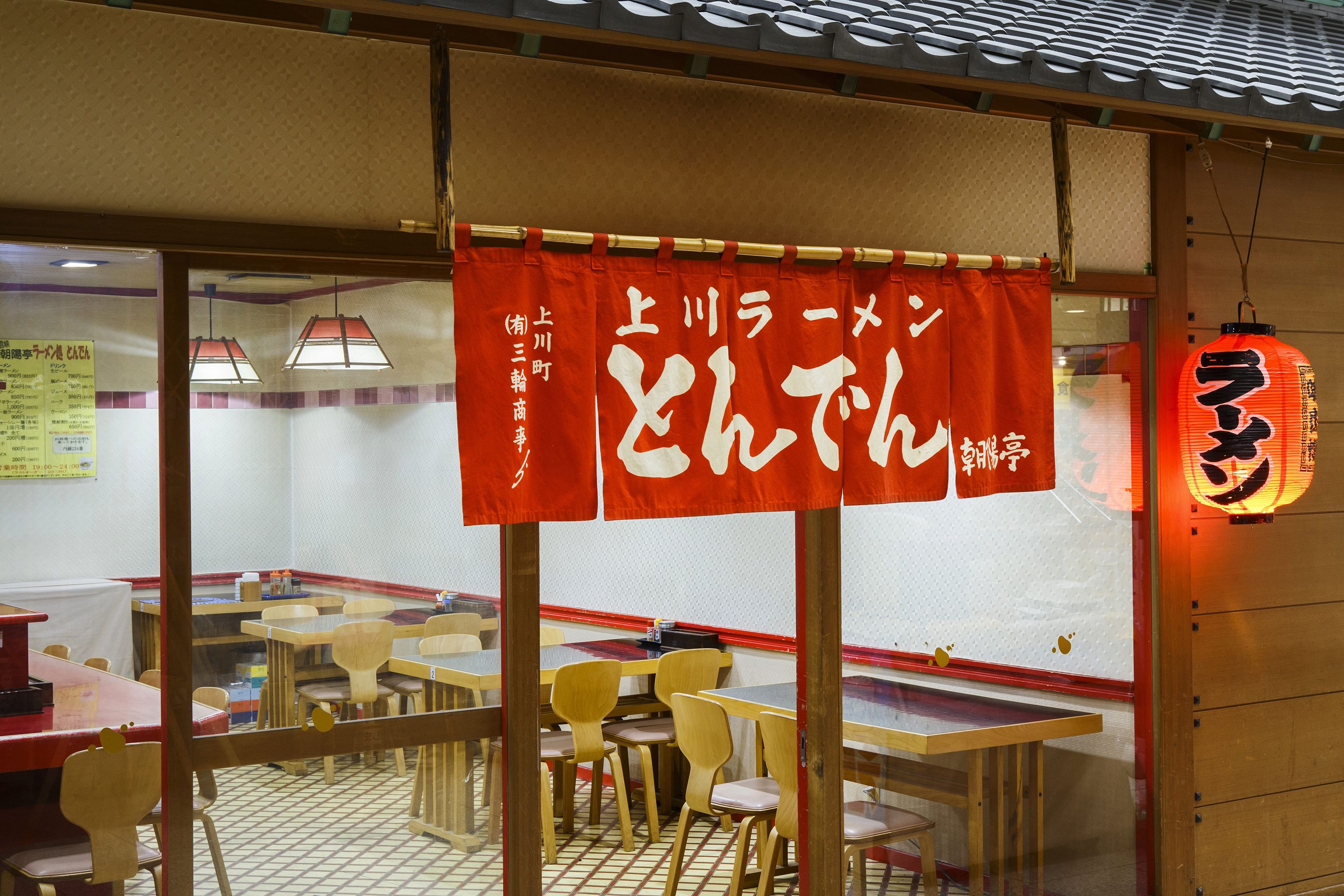 Interior de restaurante con mesas, sillas y un estandarte rojo con texto blanco.