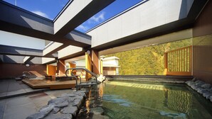 Une piscine intérieure moderne avec des marches en pierre menant à l’eau, une terrasse en bois et une vue sur une colline boisée.