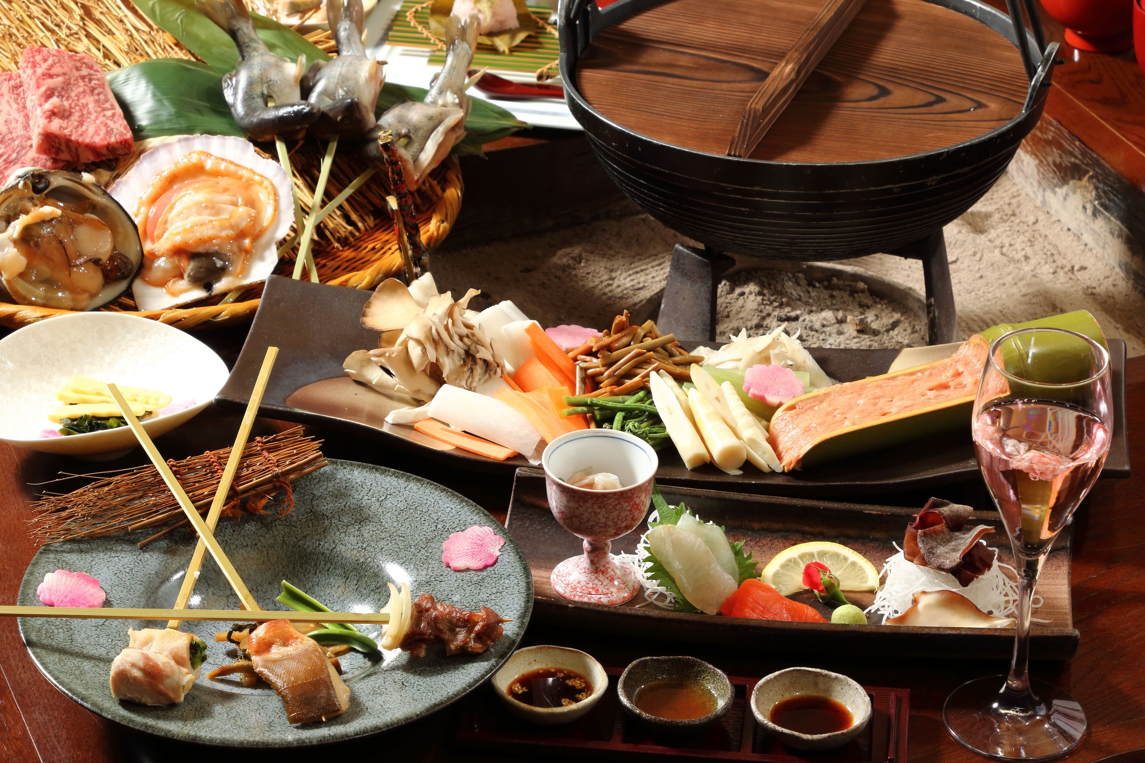 Variedad de platos y bebidas sobre una mesa de madera, incluyendo sushi, sashimi y una olla caliente.