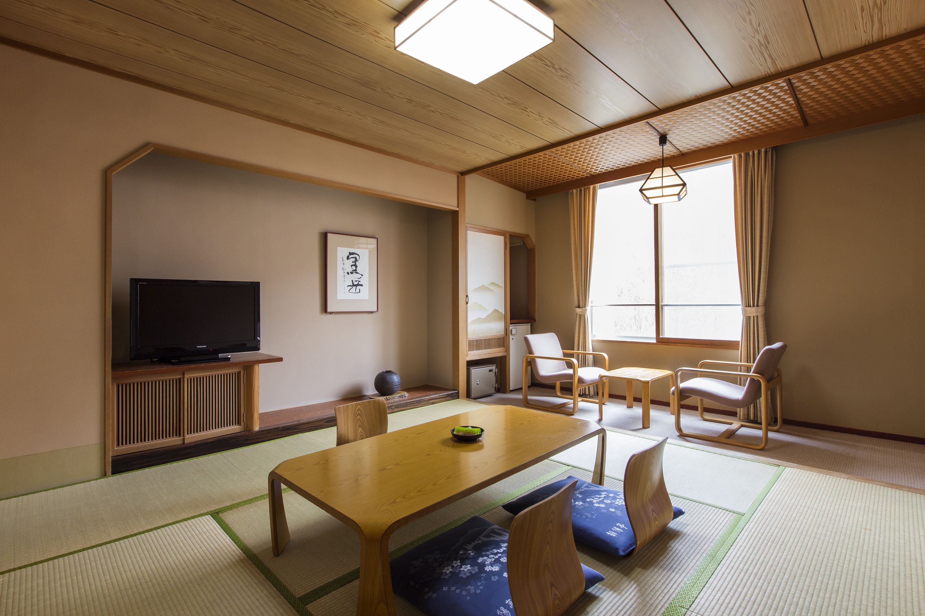 Een traditionele Japanse kamer met tatami vloeren, een televisie, een tafeltje en twee stoelen.