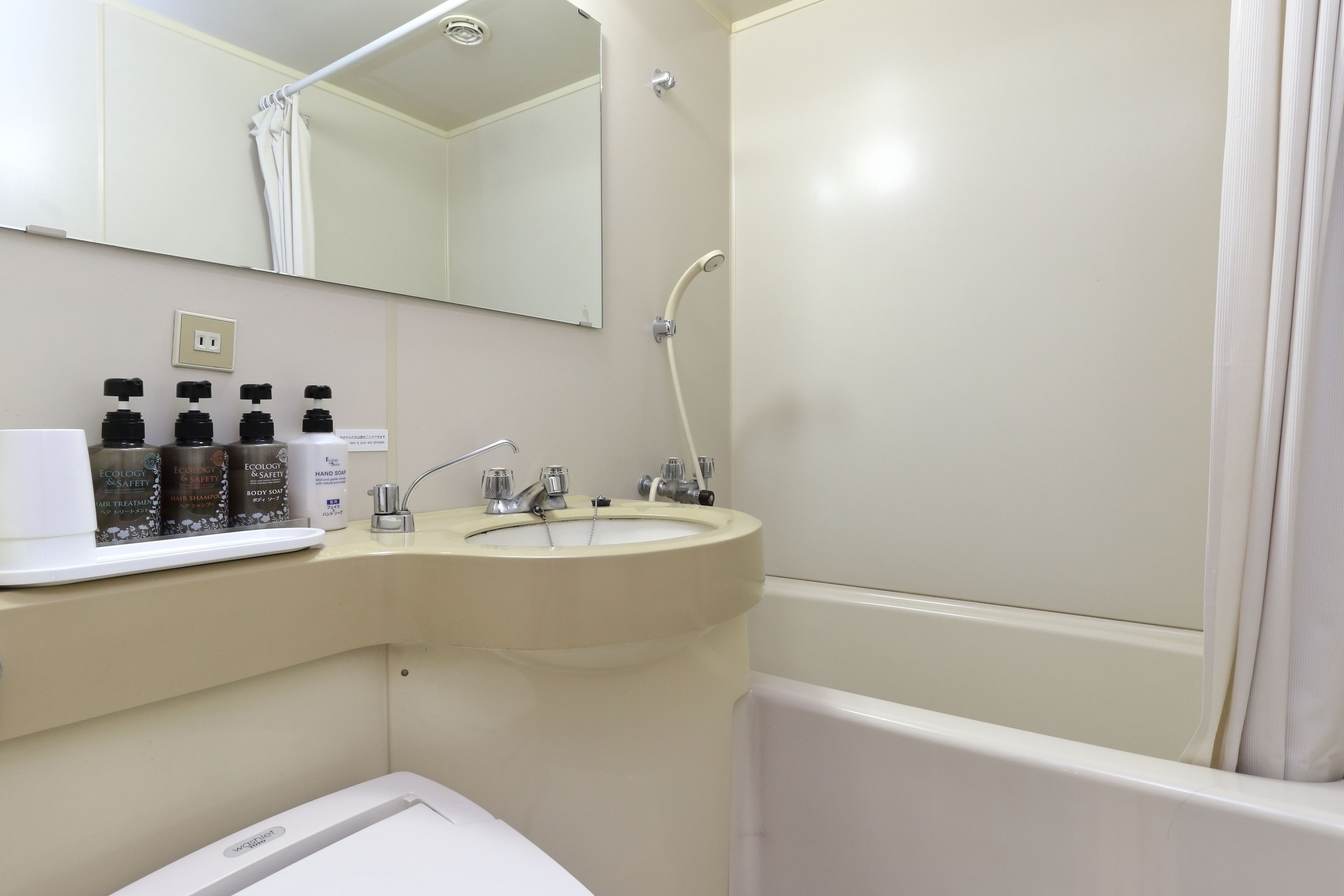 A bathroom with a sink, mirror, shower, and a shelf with toiletries.