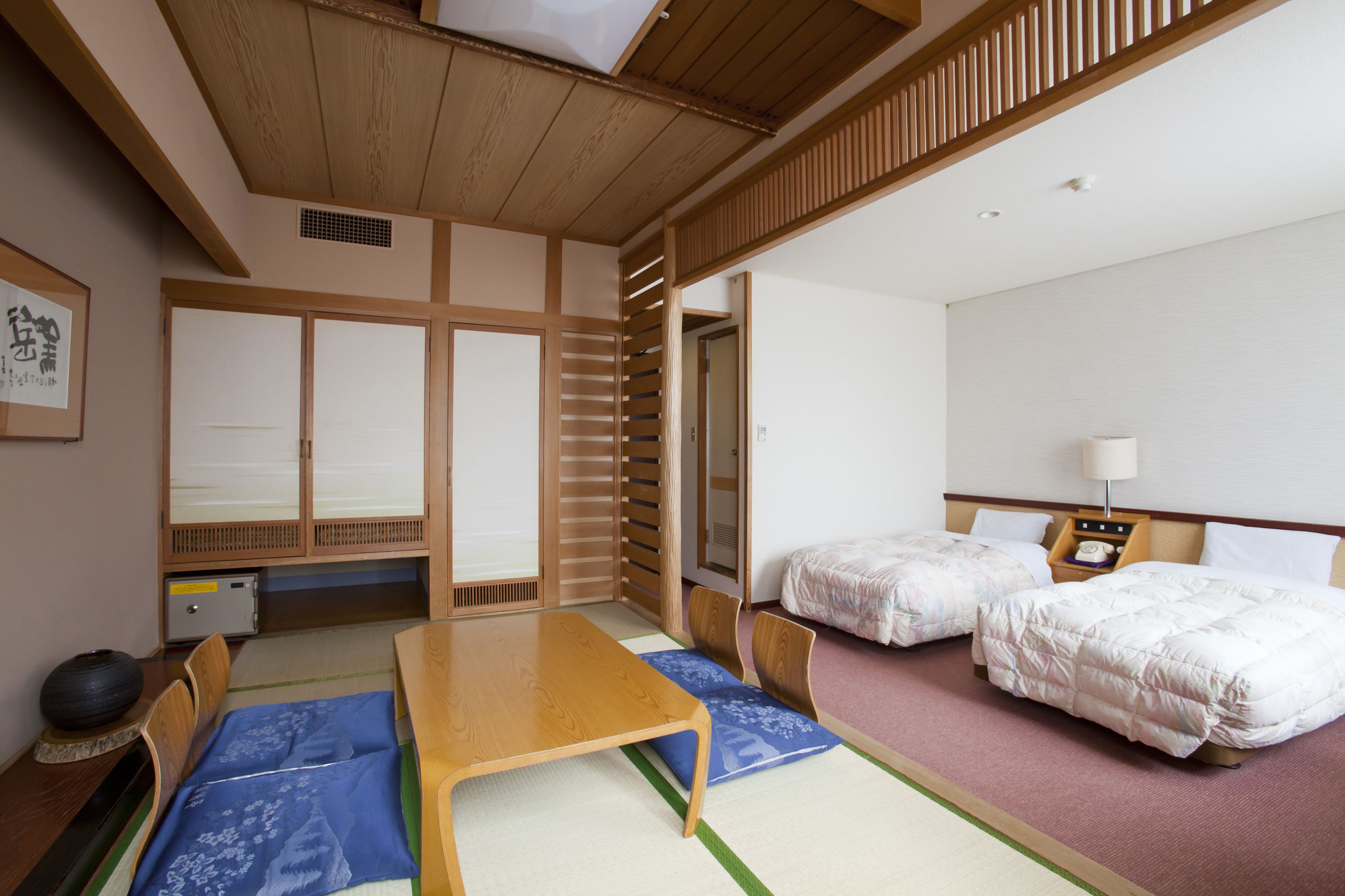 A traditional Japanese-style room with tatami flooring, a low wooden table, two beds with white bedding, and a shoji screen door.