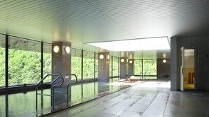 Une piscine intérieure avec des parois en verre transparent, un sol carrelé et une vue sur une zone boisée.