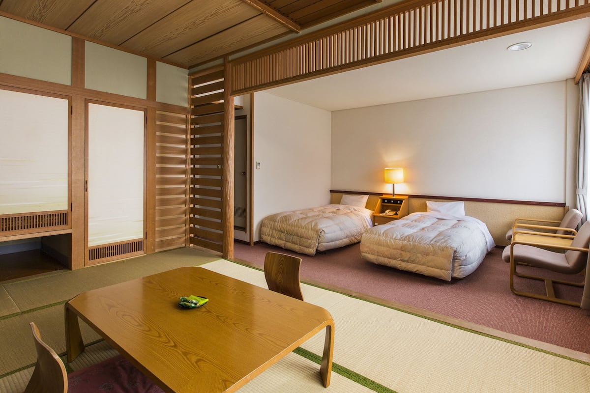 Une chambre d’hôtel avec une table en bois, deux lits, une chaise et une lampe.